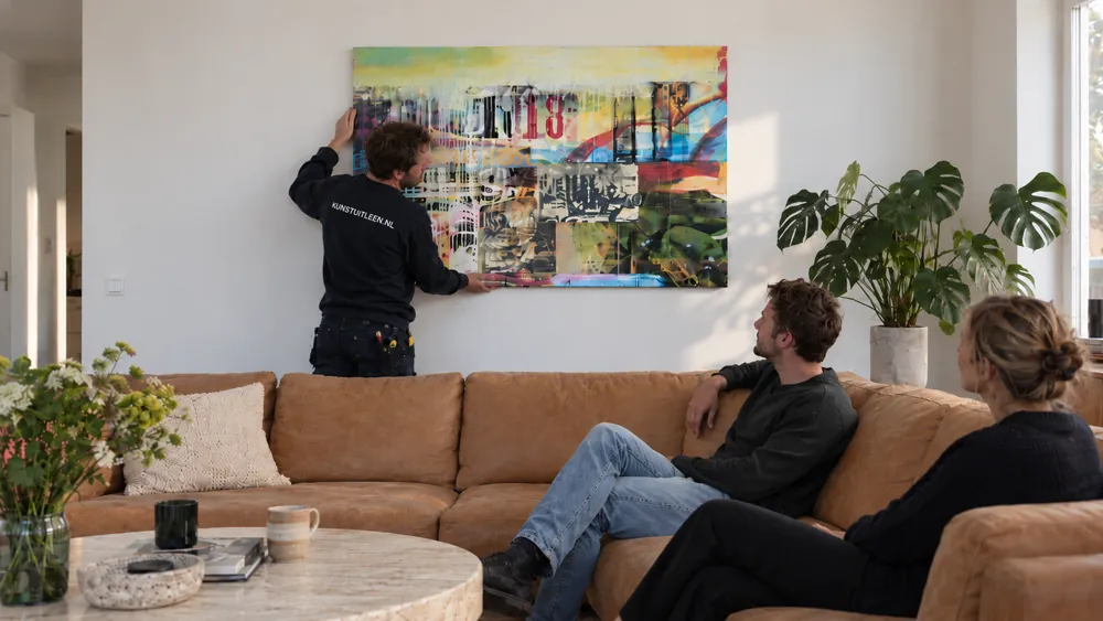 Een medewerker van Kunstuitleen.nl hangt een kunstwerk op bij klanten thuis